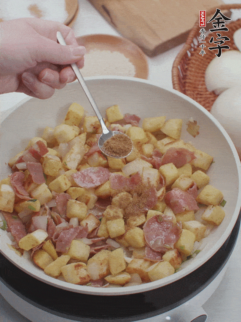 起鍋少油，煸香洋蔥丁、蔥白，加入金字培根火腿翻炒幾下，再加入饅頭丁、1小勺孜然粉、少許鹽翻炒均勻并鋪平。